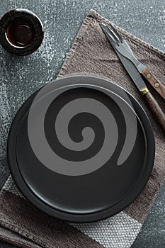Black empty plate, cutlery and napkin on stone table top view. Table setting mock up