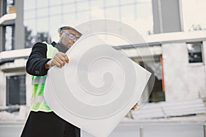 Black enginner examining building plan outdoors