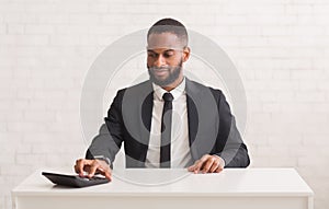 Black entrepreneur sitting at workdesk and using calculator