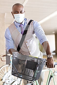 Black entrepreneurial man parking his bike. He is wearing a medical mask and formal wear