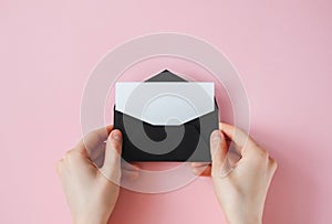 Black envelope with white blank paper in female hands on a pink background
