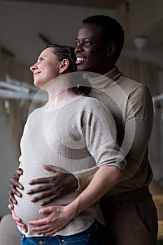 Black expectant father holding hands on belly of his caucasian pregnant wife. Mixed marriage.