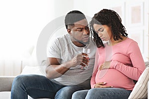 Black expecting woman feeling sick, husband giving glass of water