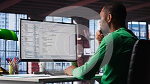 Black IT expert looking at user interface on computer at home office
