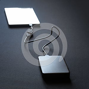 Black external hard drive connected with a wire to a smartphone, tablet or phablet. Black background photo