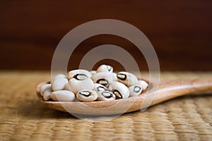 Black eyed beans in wooden spoon on reed mat