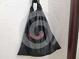 black fabric hair dryer bag on hotel wall with red text