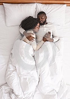 Black family couple lying and cuddling in bed, sleeping together.