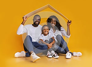 Black Family Sitting Under Symbolic Roof Dreaming Of New Home.