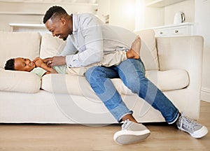 Black family, smile and a father tickling his son on a sofa in the living room of their home together. Kids, love or