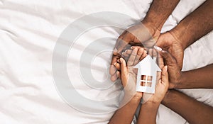 Black family of three holding paper house figure in hands