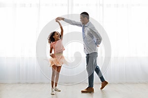 Black father and daughter dancing at home, full length shot