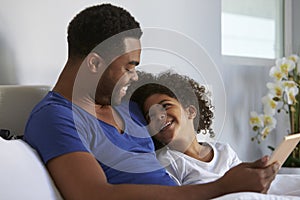 Black father and daughter relaxing in bed look at each other