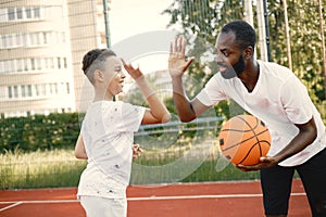 Black father with his multiracial son playing basketball in basketball court together