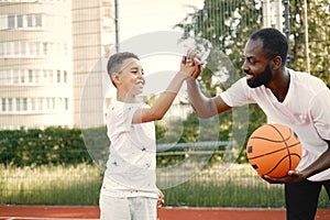 Black father with his multiracial son playing basketball in basketball court together