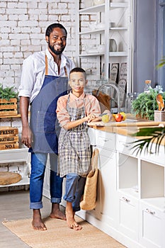 Black father and his son kid cooking fresh vegetables on kitchen at home. African dad and boy child preparing together.