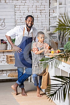 Black father and his son kid cooking fresh vegetables on kitchen at home. African dad and boy child preparing together.