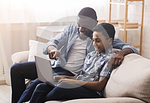 Black father and little son using laptop at home, surfing internet