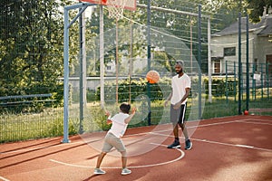 Black father with son playing basketball in basketball court together