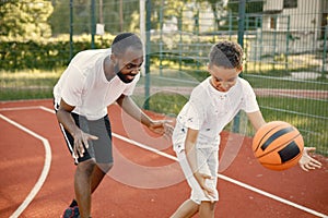 Black father with son playing basketball in basketball court together