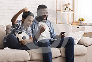 Black father and son soccer fans watching football on tv