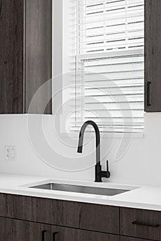 A black faucet in a kitchen with wood cabinets and white countertop.