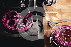 Black FDM-printer makes planetary gear machine part with visible infill from pink filament.