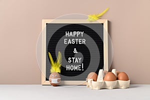 Black felt letter board with slogan - Happy Easter and Stay at Home on beige background