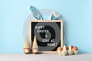 Black felt letter board with slogan - Happy Easter and Stay at Home on pastel cyan background