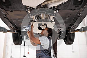 Black female auto mechanic fixing car, mechanic repairing car on lift in garage