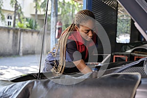 A black female automotive mechanical worker checks EV car at a fixing garage.