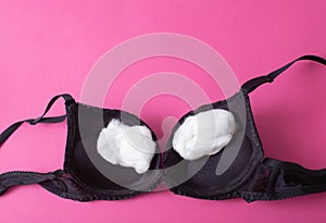 black female bra with cotton wool inside on a pink background. The concept of augmentation of the female breast with