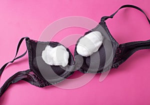 Black female bra with cotton wool inside on a pink background. The concept of augmentation of the female breast with plastic