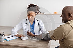 Black female doctor checking measuring pressure on patient's hand