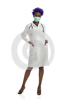 Black Female Doctor In Protective Face Mask Is Standing With Hands In Pockets. Full Length, Isolated