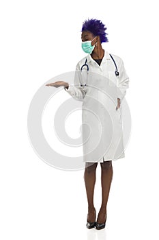 Black Female Doctor In Protective Face Mask Is Standing, Holding Hand Raised And Preseting. Full Length, Isolated