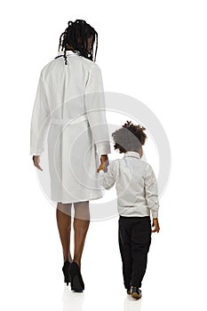 Black female doctor and small boy are walking. Rear view. Full length isolated