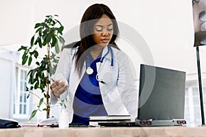 Black female doctor at work in an office, looking to laptop. Beautiful African American woman doctor or nurse working on