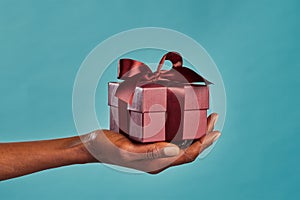 Black female hand holding gift box on blue