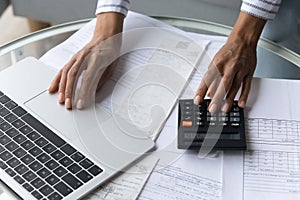 Black female hands using calculator and laptop at home office