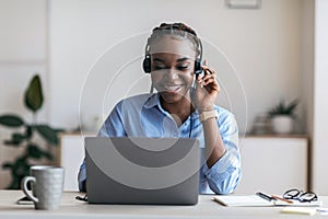 Black female manager wearing headset and using laptop in office, consulting client