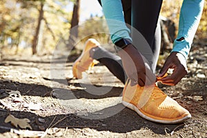 Black female runner in forest tying shoe, low section detail