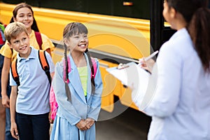 Black female teacher updating check list of children entering school bus