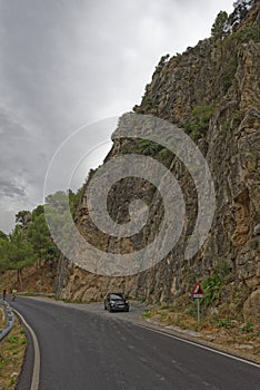 A Black Fiat Car parked in the layby of a Small Spanish Mountain Road, with two cyclists riding up the gentle hill.
