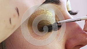 Black fine eyeliner brush applied to evening makeup in gold tones close-up view