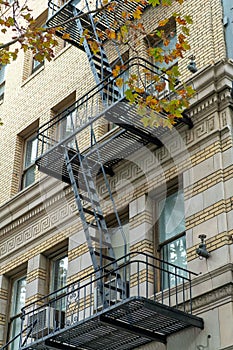 Black fire escape saftey ladder in the heart of downtown shady city with gray or beige stucco brick exterior of building