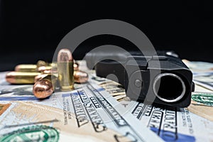 Black firearm and bullets  close-up on a pile of United States currency against a black background.