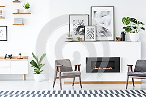 Black fireplace between grey armchairs in apartment interior wit