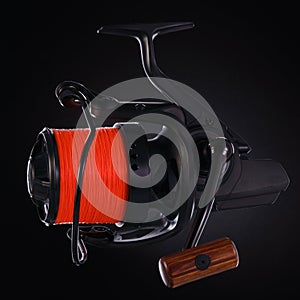 Black fishing reel with orange fishing line, on a black background. Close-up