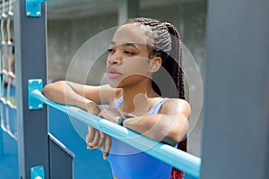 Black fitness woman looking into the distance on the sports ground, resting, taking a break between workout.